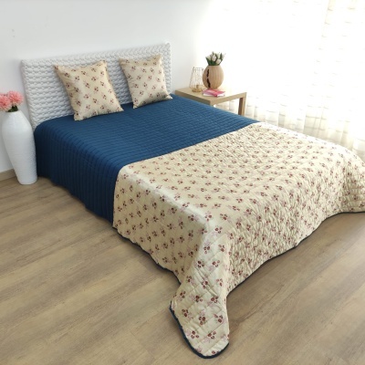 Cama com colcha reversível azul e creme com flores e almofadas correspondentes numa sala clara