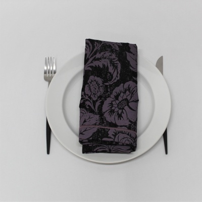 Prato branco com guardanapo roxo e preto dobrado e talheres com cabo preto à esquerda e direita.