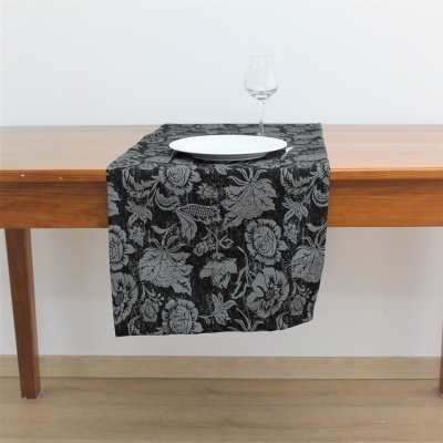 caminho de mesa preto com padrão floral cinza numa mesa de madeira clara com prato branco e taça