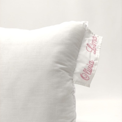 Travesseiro branco com etiqueta bordada 'Olívia Lima'