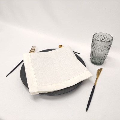 Conjunto de jantar com prato, guardanapo branco, talheres preto e dourado, e copo cinzento