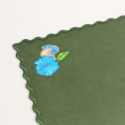 Toalhete verde com borda ondulada e bordado de flor azul