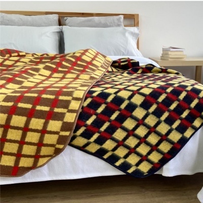 Duas mantas xadrez em cama branca com almofadas cinza e mesa com livros ao lado