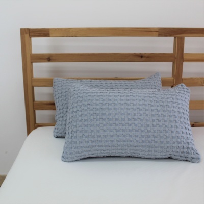 Duas almofadas de tecido azul claro com padrão texturizado sobre cama branca com cabeceira de ripas de madeira clara