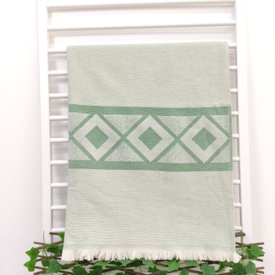 Toalha cinza claro com padrão geométrico verde e franjas na base