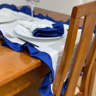 Mesa de madeira com toalha branca e azul, prato e copo, cadeira de madeira
