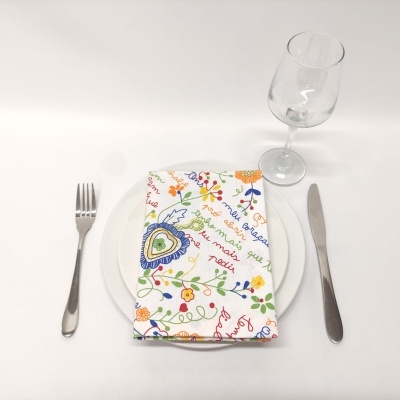 Mesa posta com guardanapo colorido sobre prato branco, talheres metálicos e copo transparente