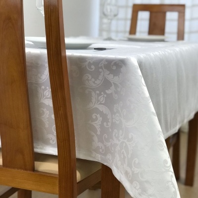Toalha de mesa branca com padrão floral sobre mesa de madeira com cadeiras