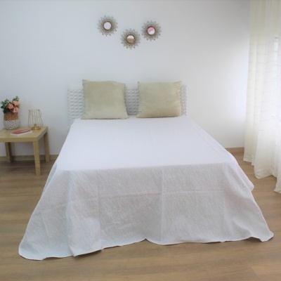 Cama de casal com roupa de cama branca e almofadas bege num quarto decorado simples