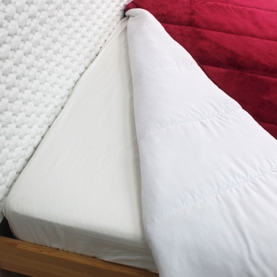 Cama com colchão branco, edredão branco e manta vermelha.
