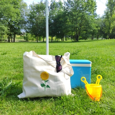 Bolsa estampada de girassol, óculos de sol, caixa térmica azul e balde amarelo na relva