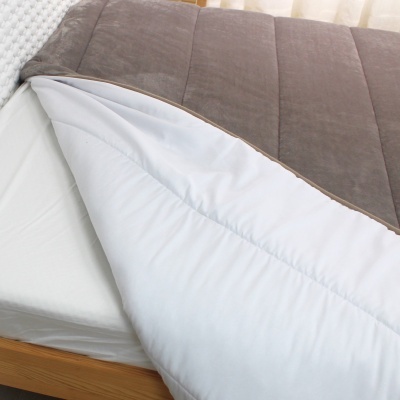Colchão branco com protetor acolchoado cinzento escuro e branco sobre cama de madeira
