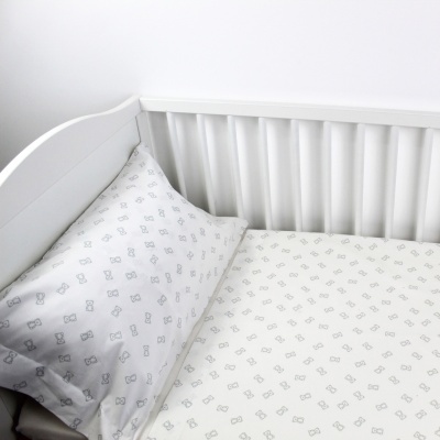 Berço branco com roupa de cama branca estampada com desenhos cinzentos pequenos.