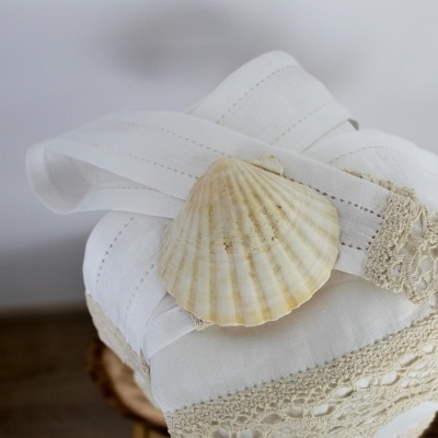 Tecidos brancos com rendas e concha marinha clara sobre superfície de madeira