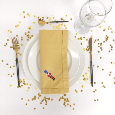 Conjunto de jantar com pratos brancos, guardanapo amarelo bordado e talheres preto e dourado