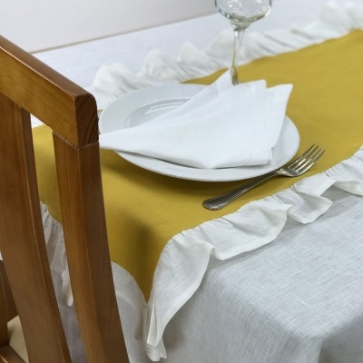 Mesa posta com toalha branca, caminho de mesa amarelo e utensílios.