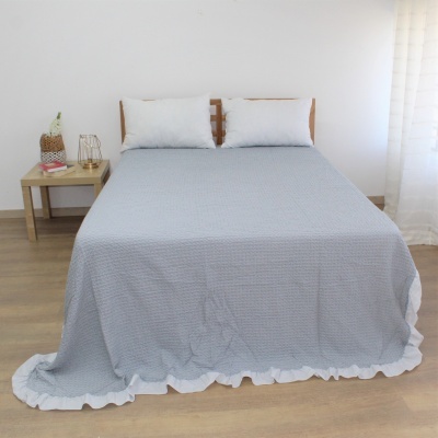 Colcha cinzenta texturizada com borda branca em cama com almofadas brancas em quarto minimalista