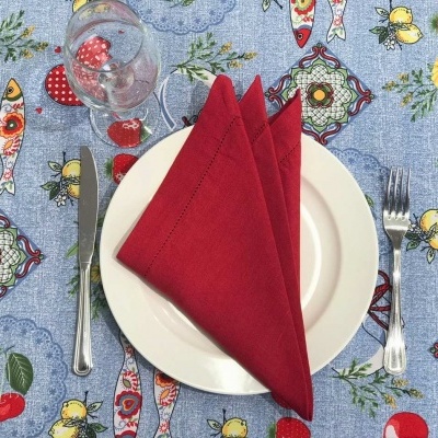 Mesa posta com toalha azul estampada, prato branco, guardanapo vermelho, talheres e copo