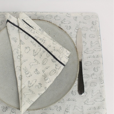 Conjunto de mesa com prato cinzento, guardanapo e toalha com padrões de coelhos e faca