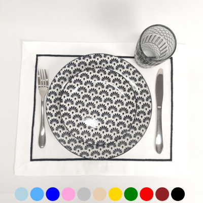 Pratos brancos com padrão preto, talheres prateados, copo de vidro e toalhete branco com borda preta
