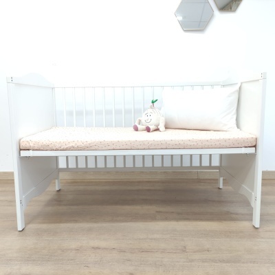 Cama de criança branca com colchão bege, almofada branca e boneco sentado