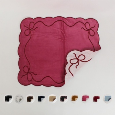 Guardanapo quadrado vermelho com bordas onduladas e padrão de laços bordados.