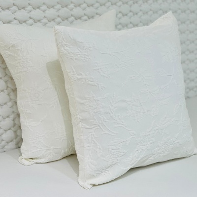 Dois almofadas brancas com padrão floral texturizado em fundo branco