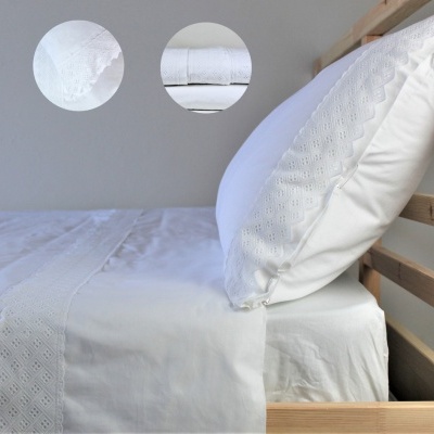 Cama com lençol e fronhas brancas bordadas em madeira clara