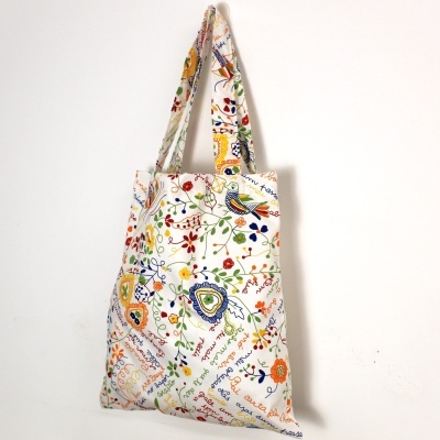 Saco de tecido branco com padrão colorido de flores, folhas e pássaros.