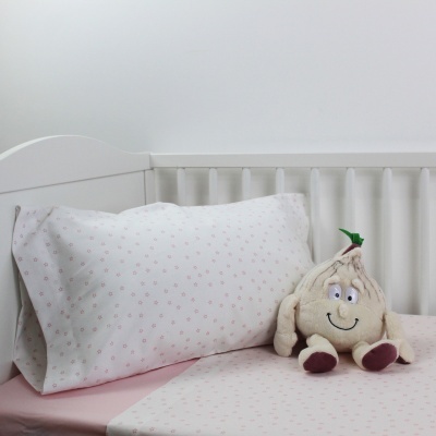 Cama de bebé com roupa de cama rosa e branca, almofada com padrão de flores e peluche de alho sorridente