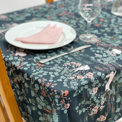 Toalha de mesa floral com figuras de coelhos, prato com guardanapo, talher e copo