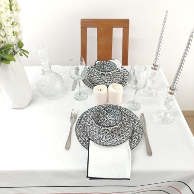 Mesa posta com aparelho de jantar floral azul e branco, taças, talheres, velas e jarro de flores brancas