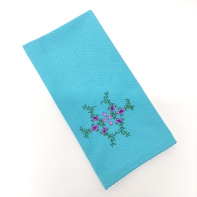 Guardanapo azul turquesa com bordado de flores roxas e folhas verdes