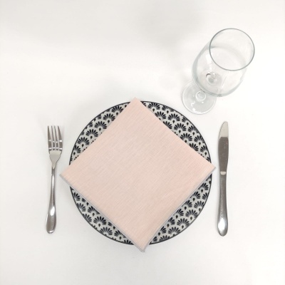 Mesa posta com guardanapo cor-de-rosa claro, prato decorado, garfo, faca e copo
