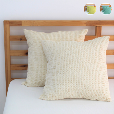 Almofadas quadradas bege claro com textura tipo palha sobre cama com cabeceira de madeira clara