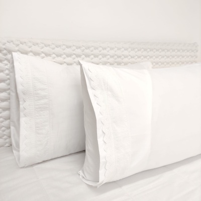 Duas fronhas brancas bordadas sobre cama com cabeceira estofada branca.