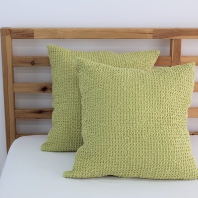 Três almofadas verdes de malha sobre cama com estrutura de madeira.