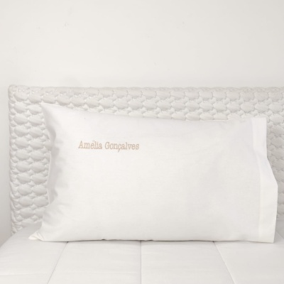travesseiro branco com bordado dourado 'Amélia Gonçalves' em cama com cabeceira acolchoada branca