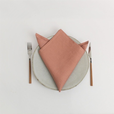 Prato com guardanapo cor de terracota, garfo e faca com cabo de madeira sobre fundo branco