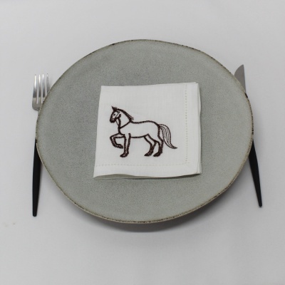Prato cinzento com guardanapo branco bordado com cavalo castanho e talheres com cabo preto