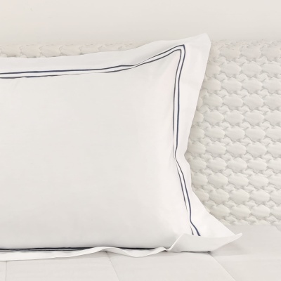 Travesseiro branco com bordas azuis sobre cama branca texturizada