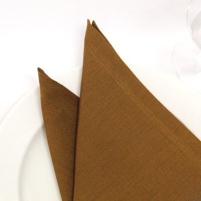 Guardanapo castanho dobrado sobre prato branco com taça à direita