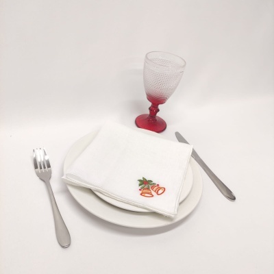 Conjunto de mesa com prato branco, guardanapo bordado, talheres de metal e copo de vidro com base vermelha