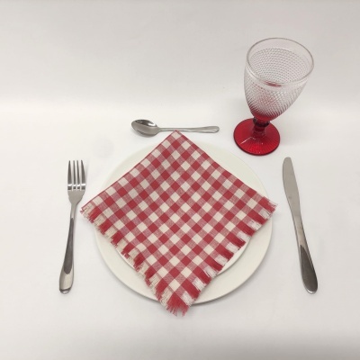 Mesa posta com prato branco, guardanapo quadriculado vermelho e branco, talheres de metal e copo de vidro com base vermelha