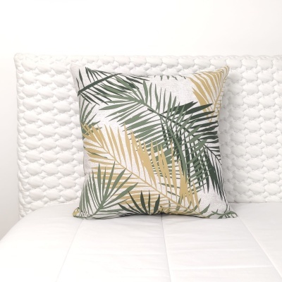 Almofada com padrão de folhas verdes e douradas sobre fundo branco