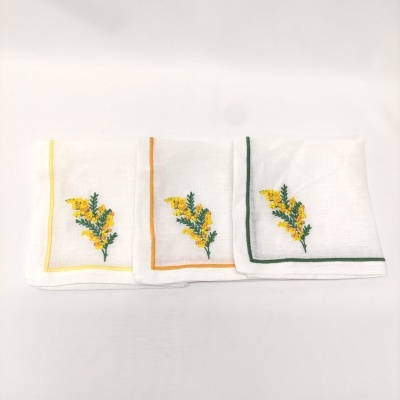 Três toalhas brancas com bordados de flores amarelas e folhas verdes, com bordas coloridas