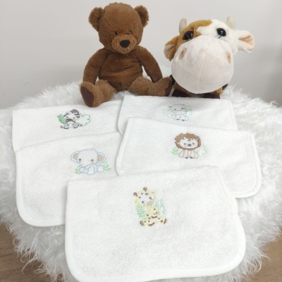 Toalhas brancas com bordados de animais e peluches de urso e vaca em fundo branco