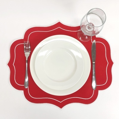 Mesa posta com prato branco, talheres de metal, copo de vidro sobre base vermelha com bordas brancas