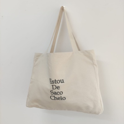 Saco de tecido cru com texto preto pendurado numa parede branca