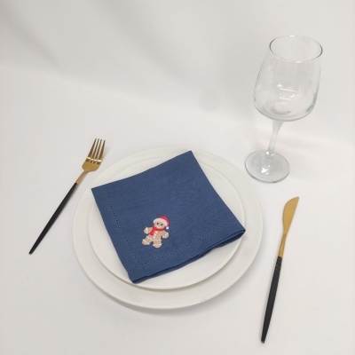 Conjunto de pratos brancos, guardanapo azul com boneco de gengibre, talheres preto e dourado e taça de vidro